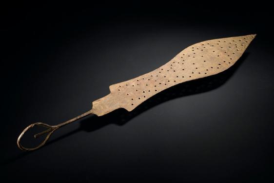 A spear shaped brass object with small holes punched on its surface. It has a thin handle with a loop at the end.