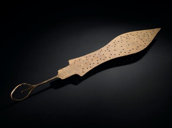 A spear shaped brass object with small holes punched on its surface. It has a thin handle with a loop at the end.