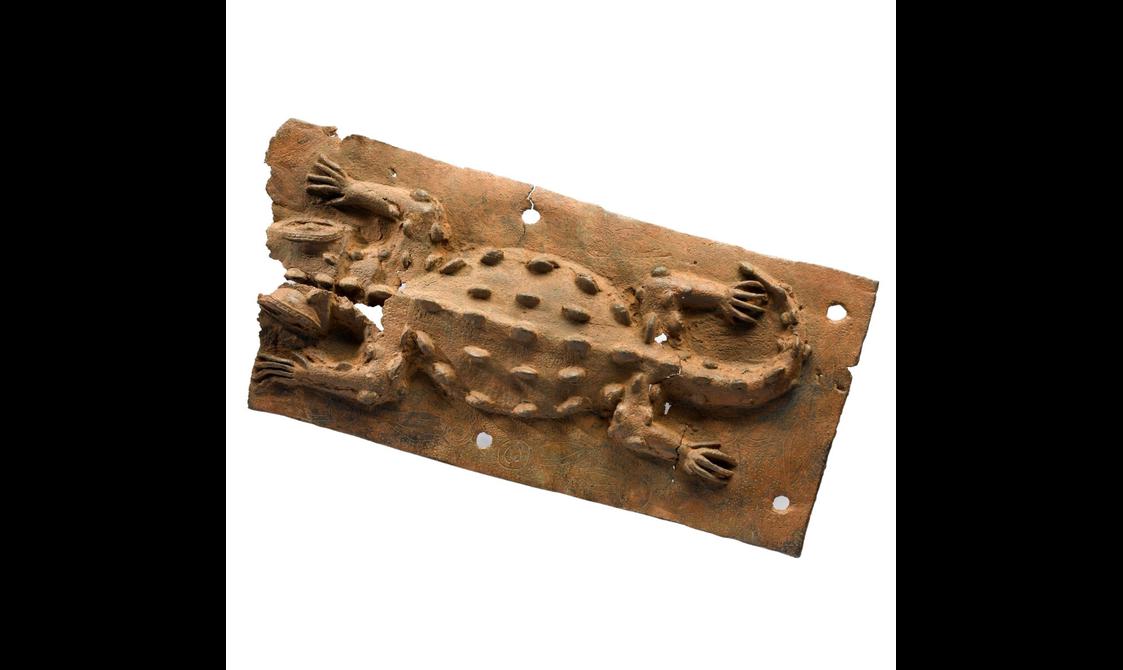 An incomplete brown sculpture with a stylised carving of a crocodile