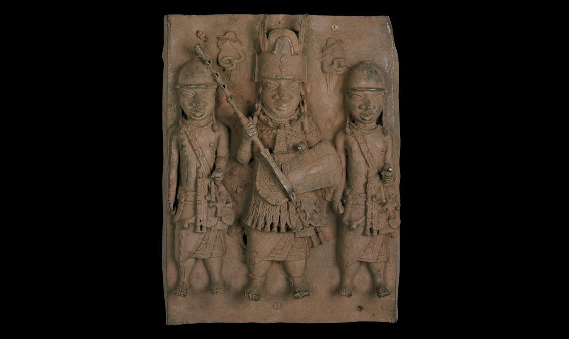 A brown rectangle sculpture with three figures carved into it. They are dressed in armor and are holding weapons.