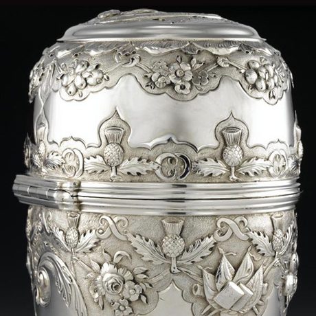 A silver lidded object decorated with thistles and flowers.