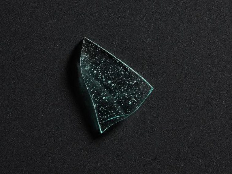 A shard of light blue glass with bubbling on its surface, against a black background