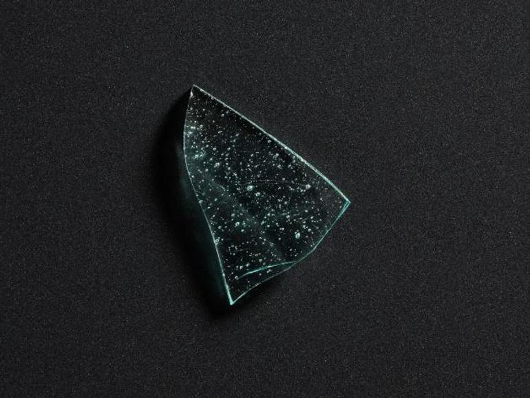 A shard of light blue glass with bubbling on its surface, against a black background
