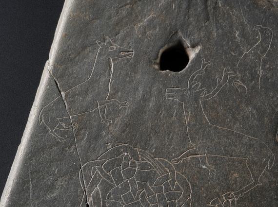 Grey stone with a small hole near the top and intricate carving of two deer.