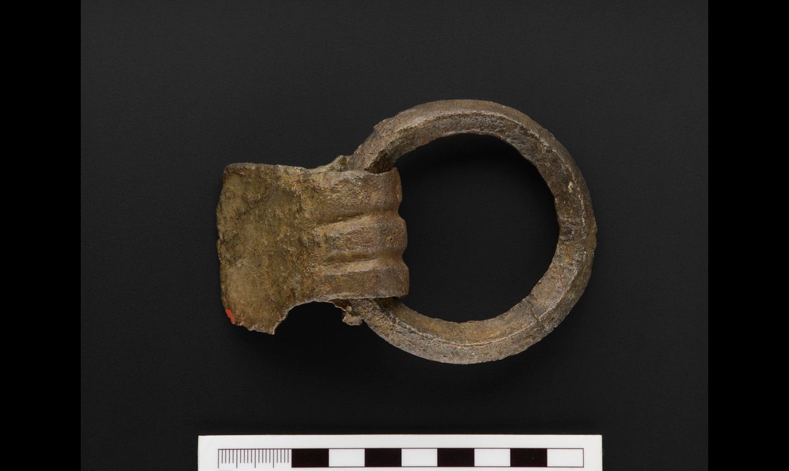 A small rusted bronze bucket handle against a black background.