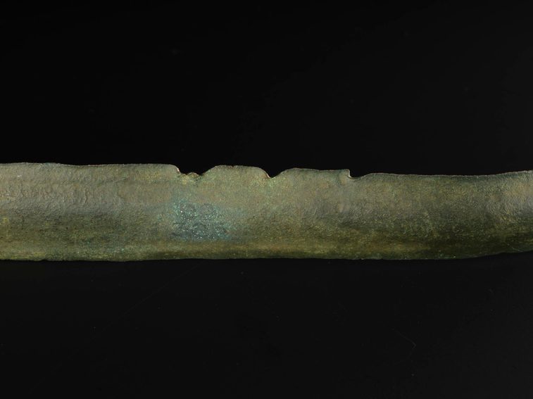 A colour photograph of a piece of bronze degraded metal on a black background.