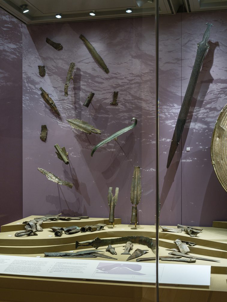 Glass display case showing a variety of bronze weapons.