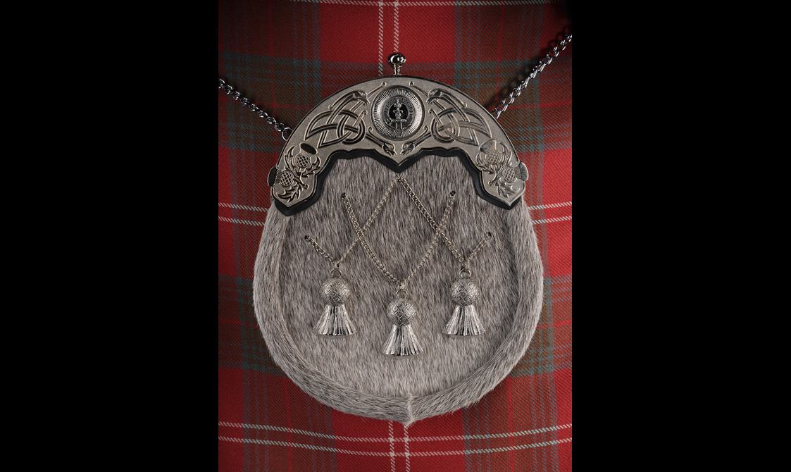 A sporran with a fur textured surface and thistle decoration, attached to a red tartan kilt.