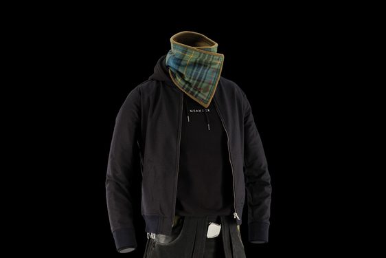 A mannequin wearing a black denim kilt, a black hoodie, a black jacket, and a green and blue tartan neck scarf.