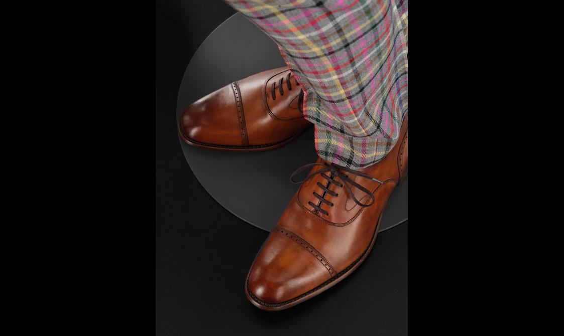 A mannequin wearing brown tan leather shoes and colourful tartan trousers.
