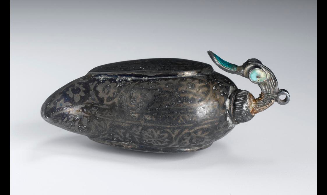 A grey container with floral decoration over its surface in an oval shape with a birds head emerging from the right.