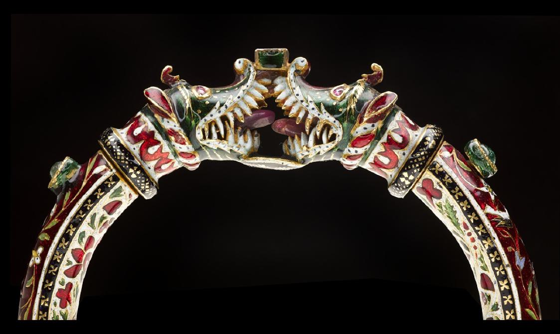A detail of a bangle bracelet showing two animal heads locking together. The bangle is highly decorative in gold, red, green, and white.