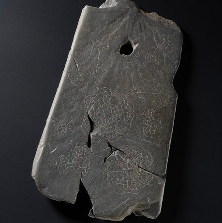 A flat rectangular grey stone with etchings of celtic knots and animals on its surface.