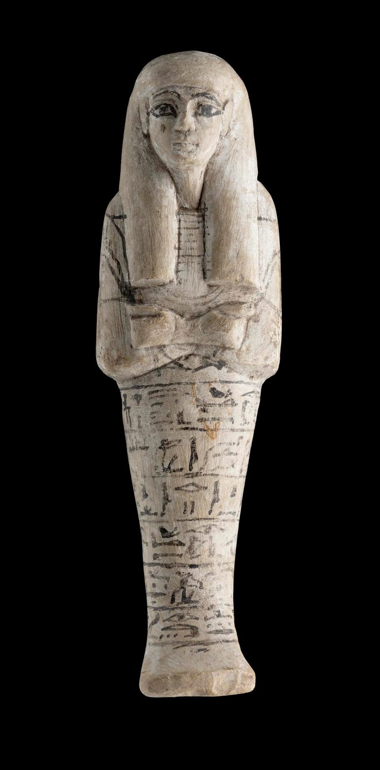A white limestone figure in the shape of a mummified person with six lines of inscription. The figure is against a black background.