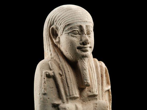 A cream-coloured mould-made ceramic figures in the shape of a mummified person, surrounded by a black background.