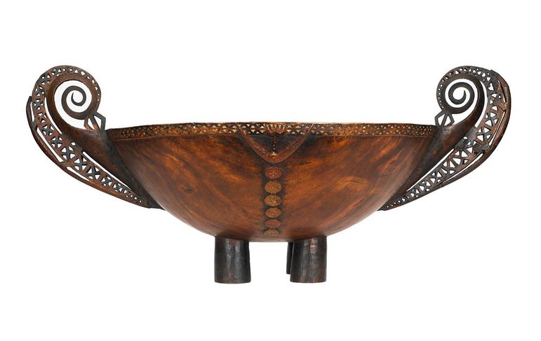 ooden feast bowl on four cylindrical feet with attached handles, carved from wood with decorative carving around rim and elaborate fretwork on handles