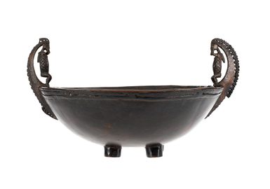 Bowl on four cylindrical feet with attached handles, carved from wood with decorative carving around rim and handles in the form of stylized figures