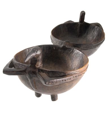 Double food bowl carved from a solid piece of dark brown wood, each half connected by two short bars, in form of a hemisphere on four feet, with a long beaked bird head at each end and two projecting openwork wings