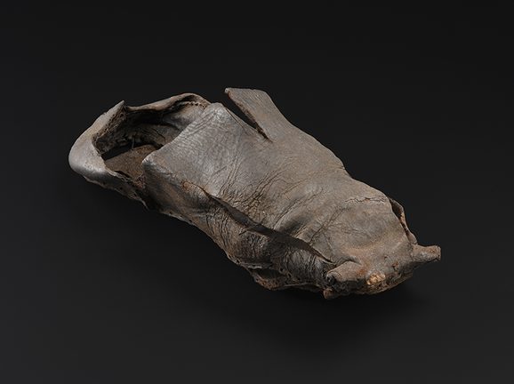 A historic black leather shoe against a black background.
