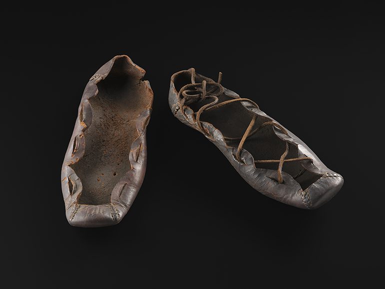 Black lace tie leather shoes in a museum storage box, stuffed with white tissue paper.