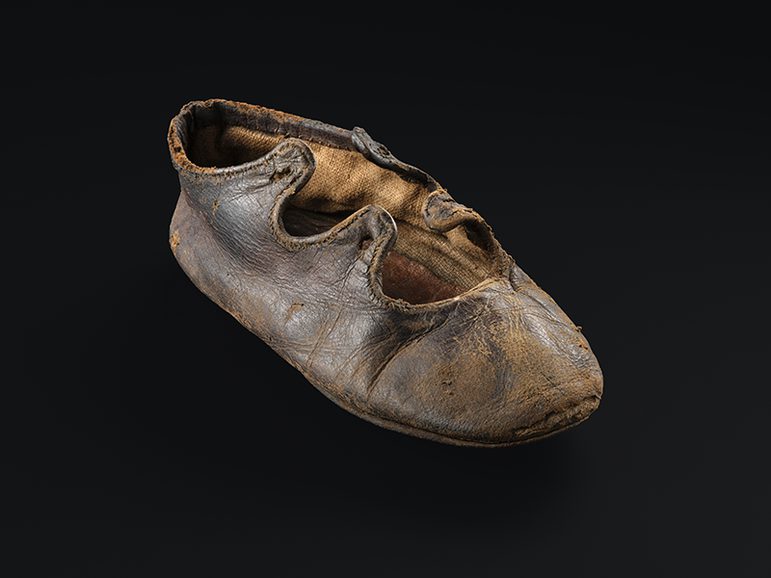 A small leather lace up shoe stuffed with tissue paper. Its laces are missing.