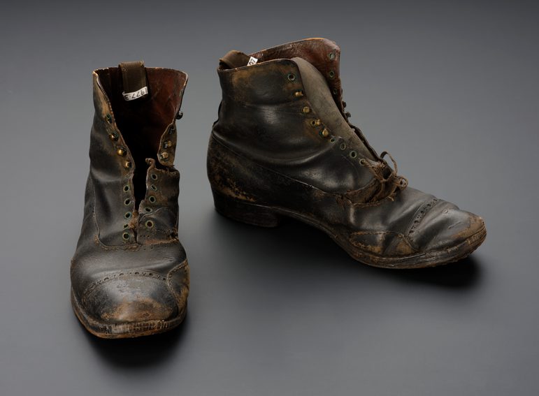 A pair of large, lace up leather boots against a grey background.