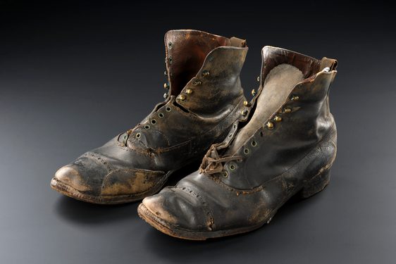 Two small, unlaced, worn dark leather ankle boots against a black and grey background.