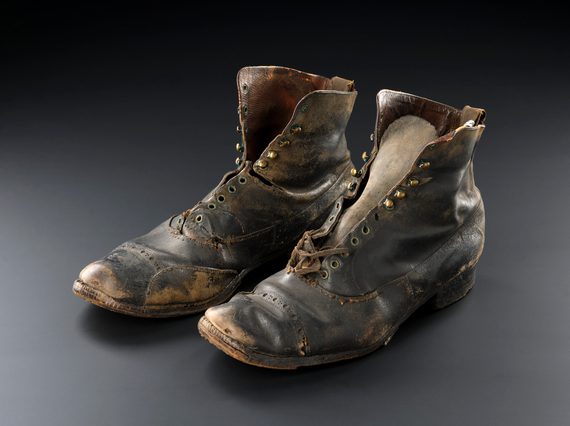 Two small, unlaced, worn dark leather ankle boots against a black and grey background.