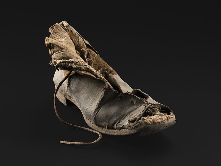 A leather shoe, badly damaged, but showing elastic and lacing.