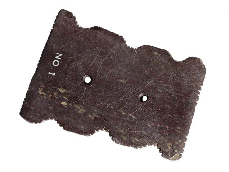 Flat oblong stone, notched on the sides and pierced with two holes,