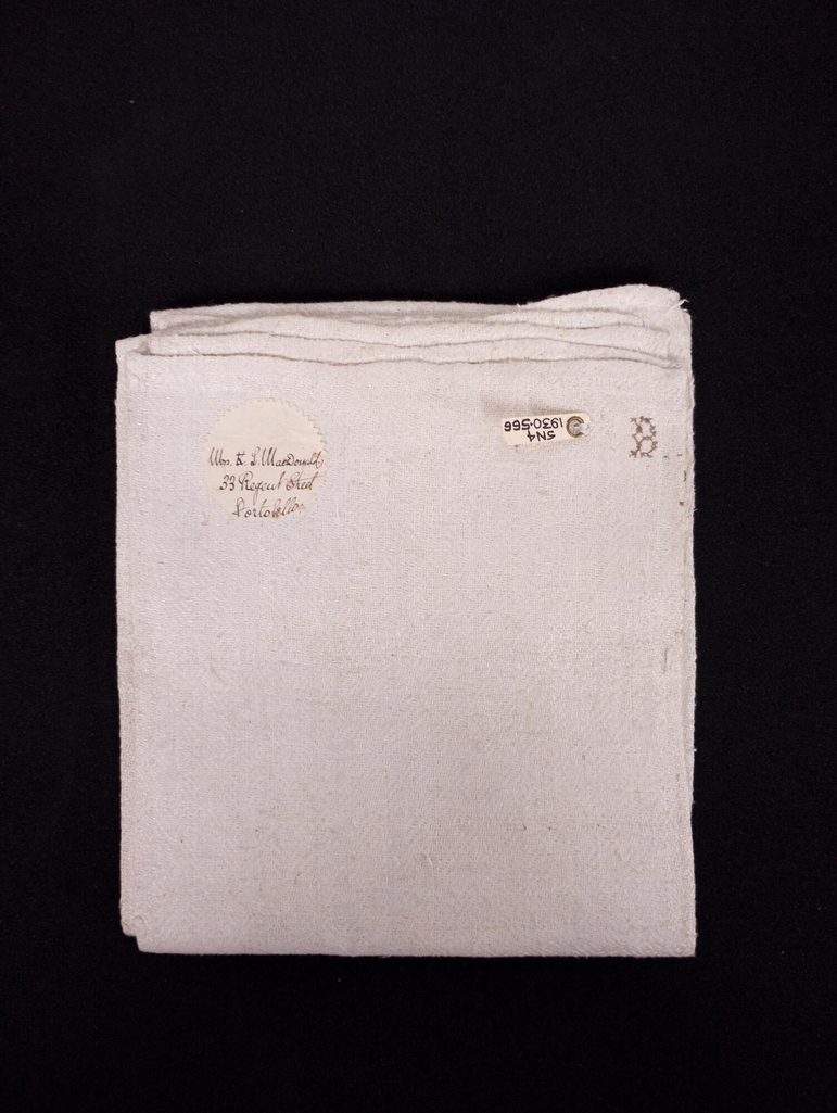 A folded white linen towel. There is a sticker in the top-left corner with a name and address on it.