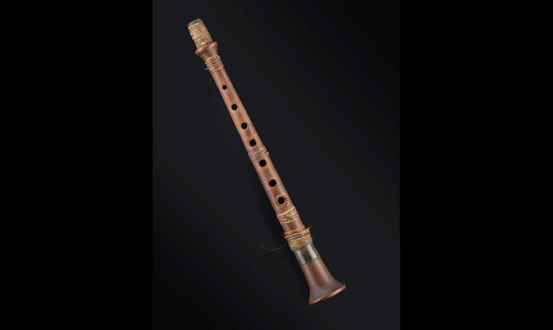 A brown wooden chanter, originally part of a set of bagpipes.