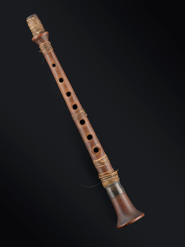 A brown wooden chanter, originally part of a set of bagpipes.