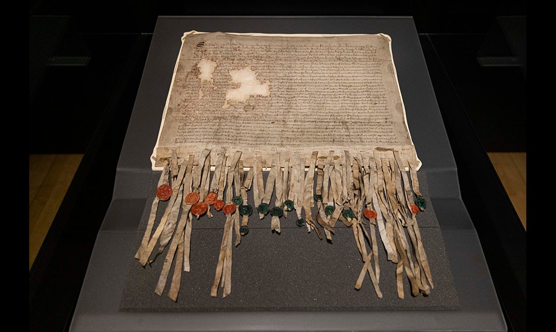 Faded paper with writing. Coloured wax seals are attached to the end of the document.
