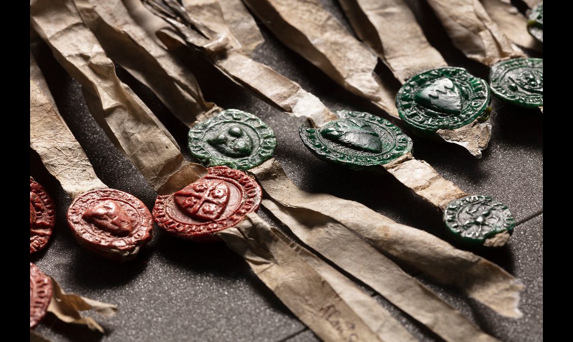 Red and green wax seals. Eeach seal has a heraldic shield surrounded by lettering.