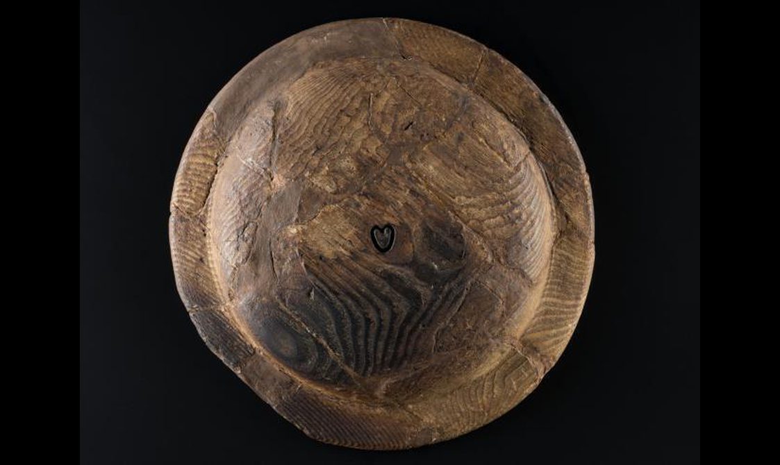 The reverse of a wooden plate. There is a small engraved heart in the centre of the bowl.