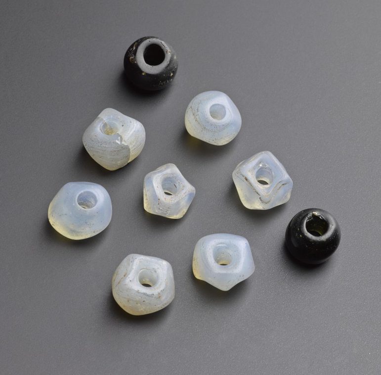 A selection of black and transparent glass beads against a grey background. The beads are arranged in a diamond grid formation.
