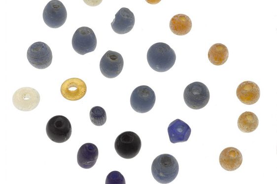 A set of multicoloured glass beads arranged on a white background. The collection are if blue, grey, black yellow and white and arranged in a diagonal grid.