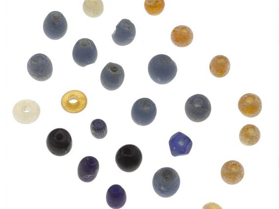 A set of multicoloured glass beads arranged on a white background. The collection are if blue, grey, black yellow and white and arranged in a diagonal grid.