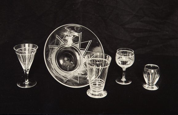 5 cut glass objects against a black background,. There is a wine glass, a graphically etched bowl, a beer glass, another wine glass and a goblet.