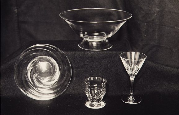 4 cut glass objects against a black background. There is a wide fluted bowl, a twisted design bowl, a cut etched goblet and an etched wine glass.