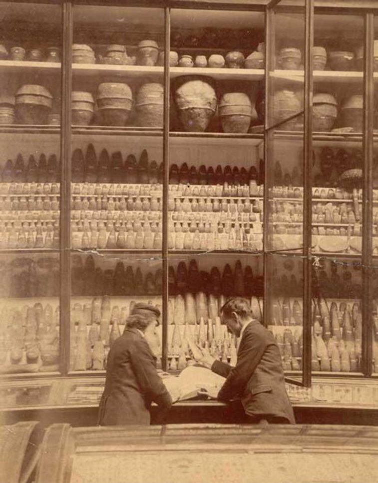 A sepia toned photograph of two adults beside a collection of museum objects