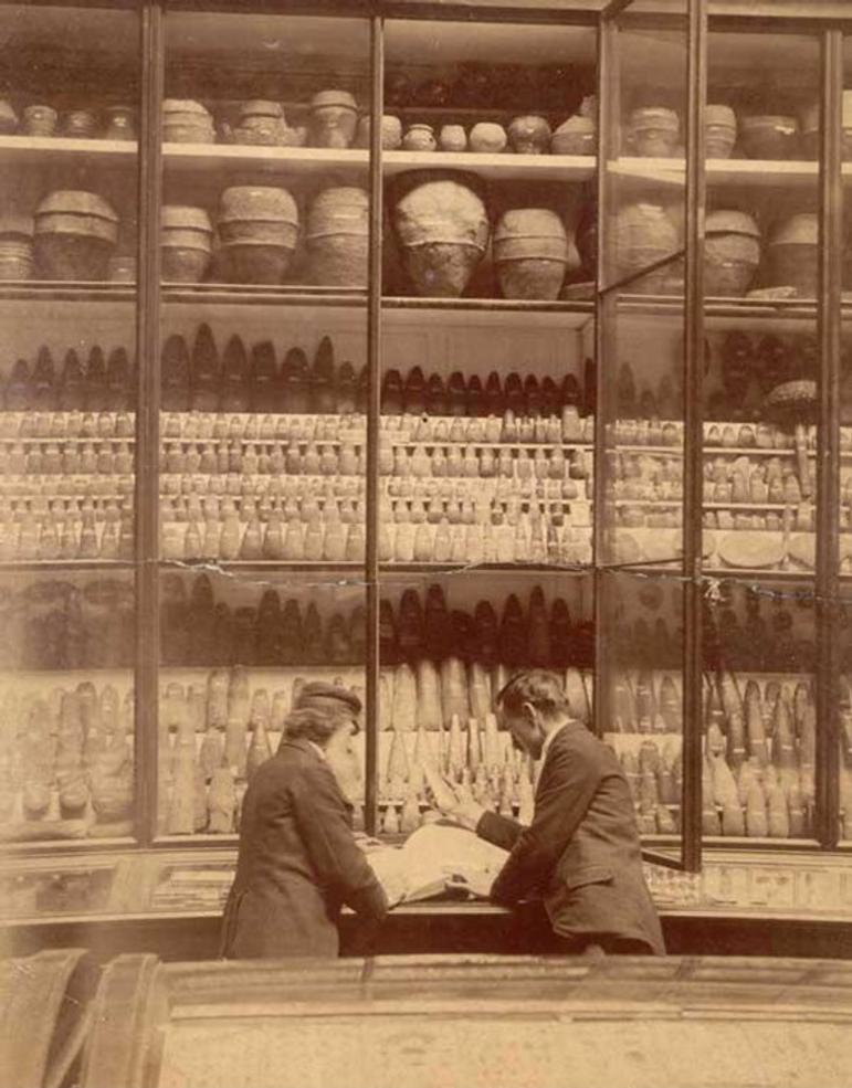 A sepia toned photograph of two adults beside a collection of museum objects
