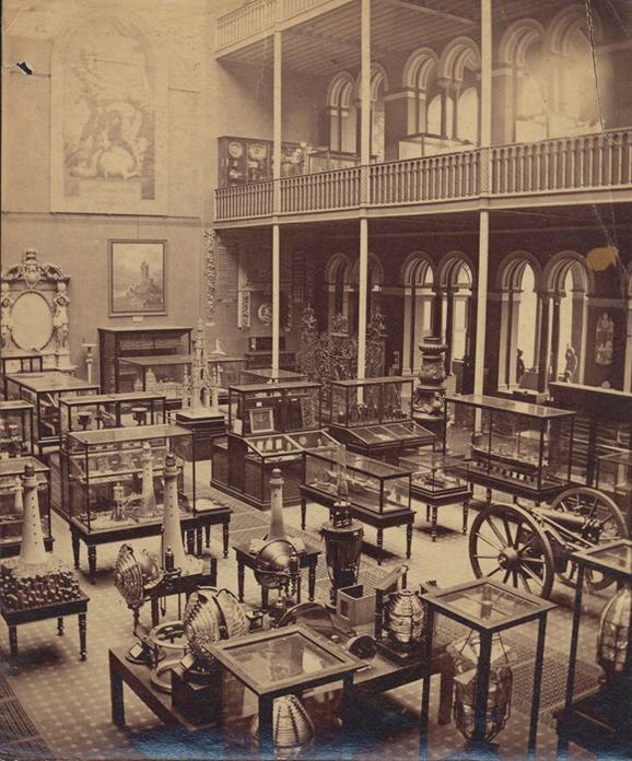 A sepia toned photograph of a Victorian-age museum hall filled with exhibition cases