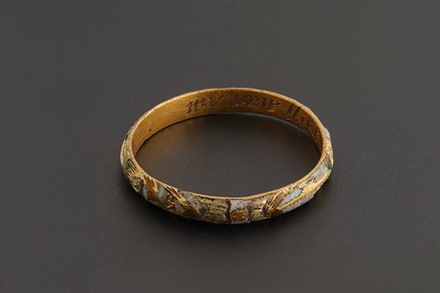 A gold ring with enamel flowers and markings. Inside the band there's the first part of an inscribed phrase 'My love like this' in sight.