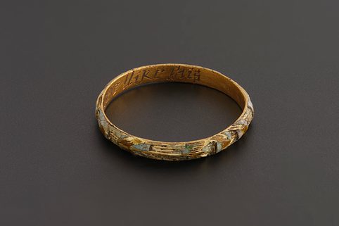 A gold ring with enamel flowers and markings. Inside the band there's the first part of an inscribed phrase 'My love like this' in sight.