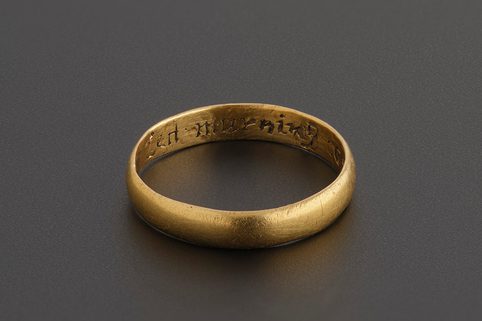 A simple gold ring against a dark grey background. 'Lett murning' inscription from the phrase 'lett murning cease and love increase' on the inside of the band.