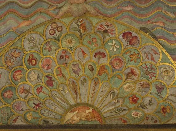 A detail of a painted wooden surface in gold, green, pink, and blue colours painted in a fanned petal like pattern