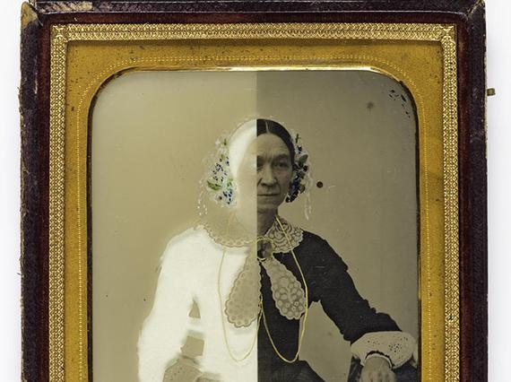 A black and white image of a woman in Victorian dress with half of the image in a white negative. The photograph has a gold border and wooden frame.