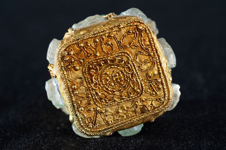 The golden base of a jar, turned to face forward. Golden lines form letters going around the base's square edges.